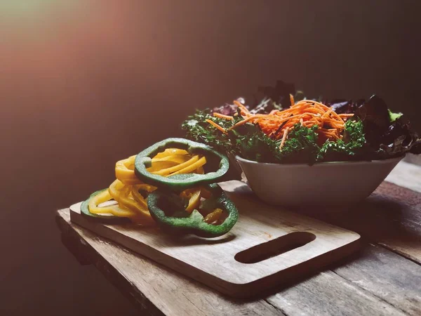 stack of sliced bell peppers and salad bowl on table edge