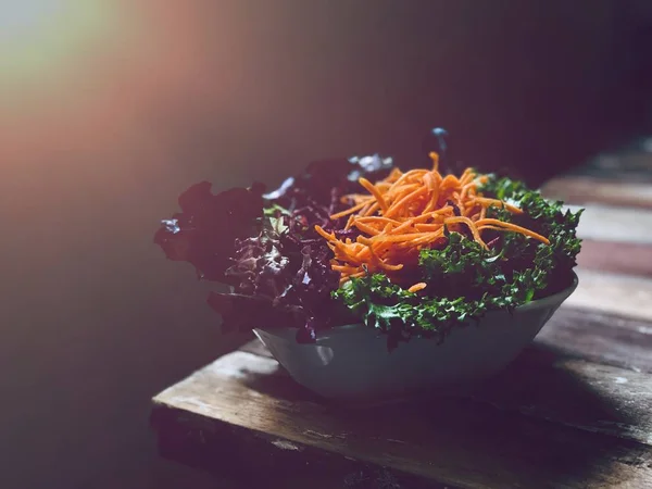 fresh salad bowl on table edge in low light