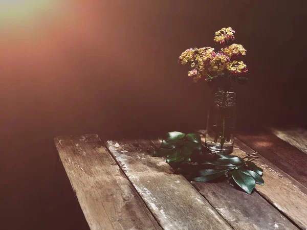 vase with bouquet on rustic wooden table in low daylight