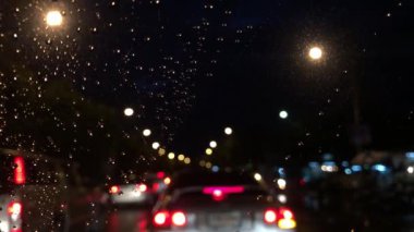 Araba ön camına düşen yağmur damlaları. Yağmurlu bir fırtına şehirde trafik ile renkli bokeh. Ağır yağmurlu günde araba sürüş, bulanık ışık arka plan. Seçici odak.