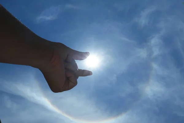 silhouette of male hand raising into solar halo on bright sky with white fluffy clouds, Solar energy concept