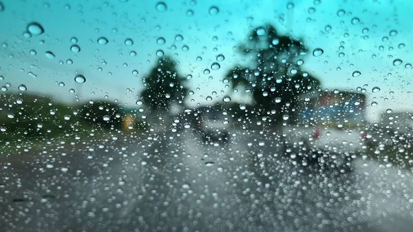 Raindrops on car windshield, blurred light background, traffic in the city on rainy day, colorful bokeh.