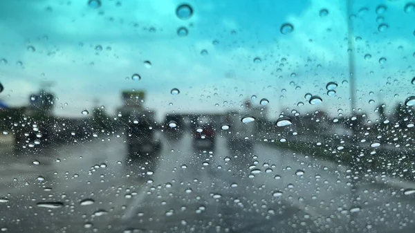 Raindrops on car windshield, blurred light background, traffic in the city on rainy day, colorful bokeh.