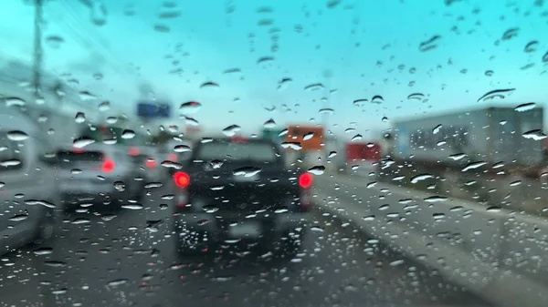 車のフロントガラスに雨滴 ぼやけた光の背景 雨の日に街のトラフィック カラフルなボケ — ストック写真