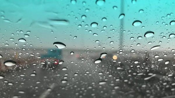 Raindrops on car windshield, blurred light background, traffic in the city on rainy day, colorful bokeh.