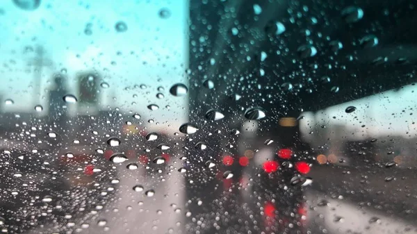 Yağmur damlaları araba ön cam, bulanık ışık arka plan, yağmurlu bir gün şehirde trafik, renkli bokeh.