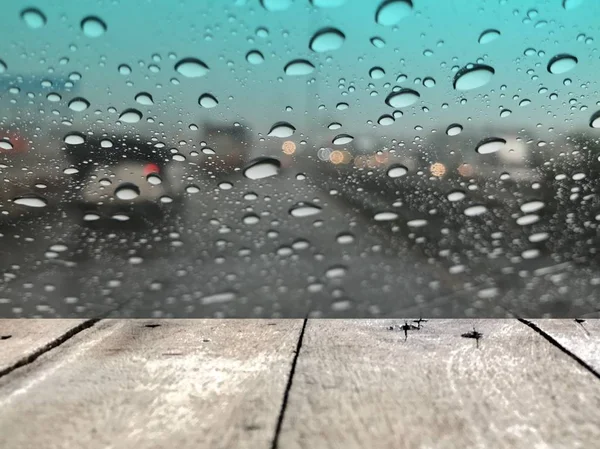 雨の日に雨の日に街の交通とぼやけた通りの背景に雨滴と車のフロントガラスの前に木製の板 — ストック写真
