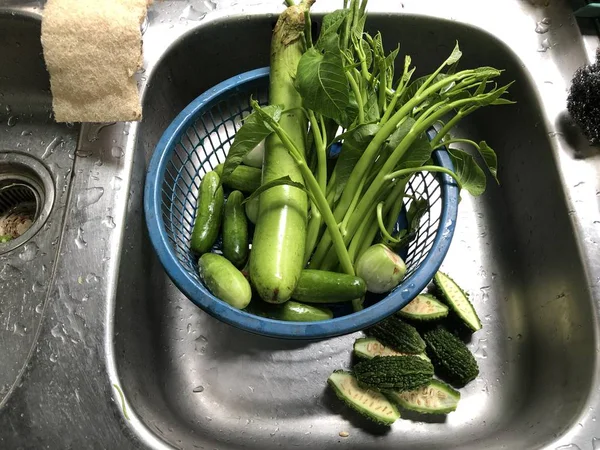 close up of greens and vegetables in plastic basket at kitchen