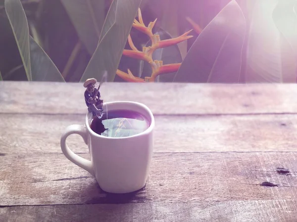 Relaxation in coffee time.Black coffee in white mug,Miniature of fisherman sitting and fishing, relaxed on the cup edge, in Americano coffee,free space for your text, with lens flare, selective focus.