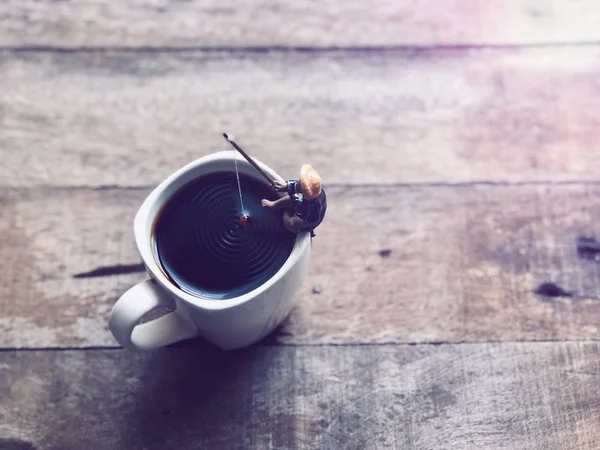 Relaxation in coffee time.Black coffee in white mug,Miniature of fisherman sitting and fishing, relaxed on the cup edge, in Americano coffee,free space for your text, with lens flare, selective focus.