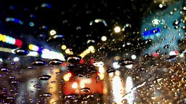 Defocused image,colorful bokeh with street light at night,raindrop on car windshield.Driving car in heavy rain storm.Traffic in the city on a rainy day.