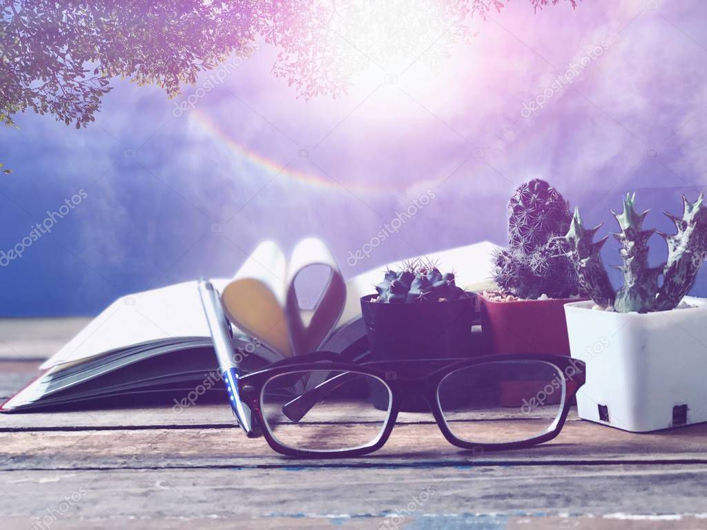 Eyeglasses,Cactus in small pots,blur Book page rolls,like shaped heart on wood table,blur beautiful nature scene as outside view,with lens flare,selective focus.