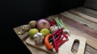 Organik sağlıklı sebzeler. Kırmızı biber, limon, fesleğen yaprağı, limon çimeni, kaffir kireç yaprakları kırsal mutfakta eski ahşap bir kalas üzerinde ve loş bir ışık, lens alevi ve metin tasarımı için yer var. Seçici odak.