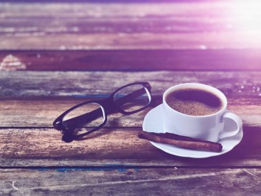 Ahşap masanın üstünde beyaz kahve fincanı, sade yaşam, yumuşak koyu ton, loş ışık, lens alevi, metin için boş alan. Kahve zamanı rahatlama kavramı