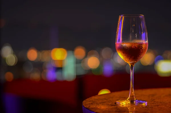 A glass of Rose wine with bokeh light at Bangkok city and colorful light from rooftop bar.