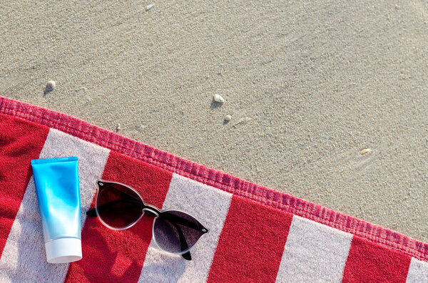 Sunglasses with sunscreen lotion and bag on red towel.