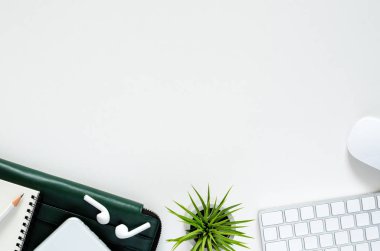 Kablosuz klavye ve fare ile modern işyeri, kablosuz kulaklık ile akıllı telefon, kalem, Notebook, yeşil belge çantası ve beyaz arka planda tillandsia Hava tesisi.