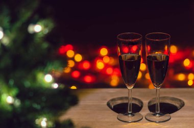 İki kadeh gül şarabı ahşap masada Noel ağacı ve renkli bokeh ışıklı arka plan.
