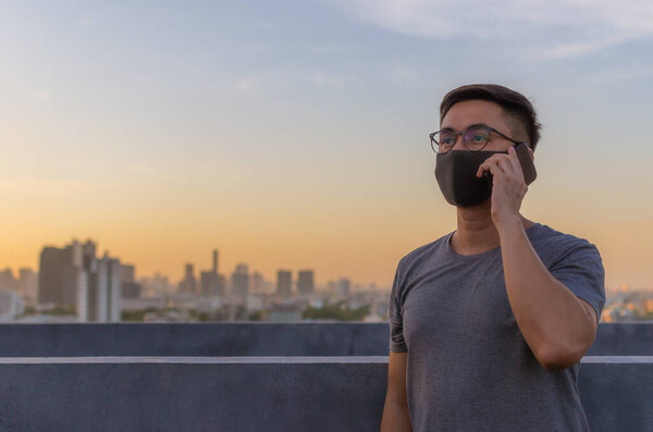 Asian man wearing face mask to protect from virus and make a call with smartphone.