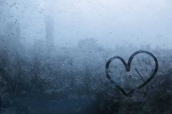 Heart painted on window which fogged up with blurred city background.