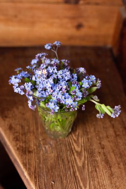 Ahşap bir arka planda cam bir fincanda mavi kır çiçekleri. Unut beni..