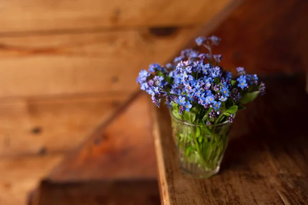 Flores silvestres azules en una taza de vidrio sobre un fondo de madera. No me olvides. . — Foto de Stock
