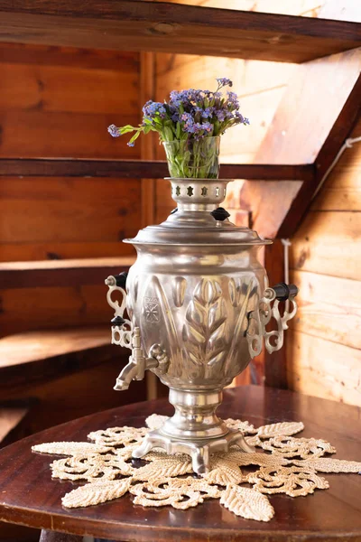 Antiguo samovar de metal y un ramo de flores azules sobre un fondo de madera — Foto de Stock