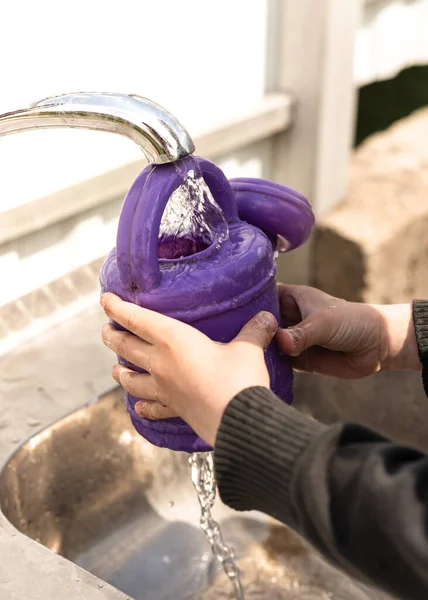 Anak itu menuangkan air dari keran ke dalam kaleng air ungu — Stok Foto