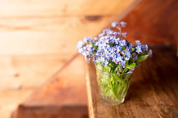 Flores silvestres azules en una taza de vidrio sobre un fondo de madera. No me olvides. . — Foto de Stock