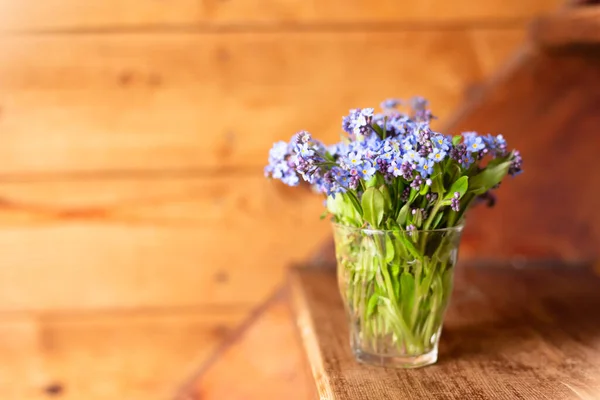 Flores silvestres azules en una taza de vidrio sobre un fondo de madera. No me olvides. . — Foto de Stock