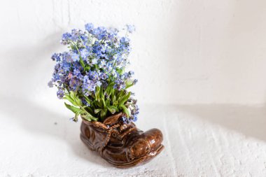 Beyaz arka planda bir buket unutmabenekli seramik terlik.