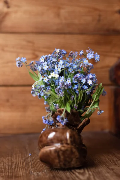 Ramo de flores no me olvides flores en un jarrón de cerámica sobre un fondo de madera. — Foto de Stock