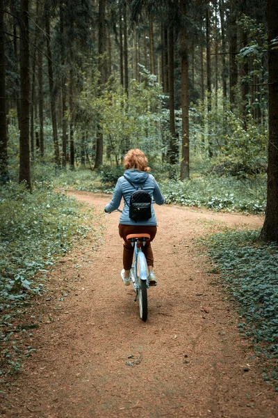 Une femme roule au loin le long d'une route forestière sur un vélo — Photo