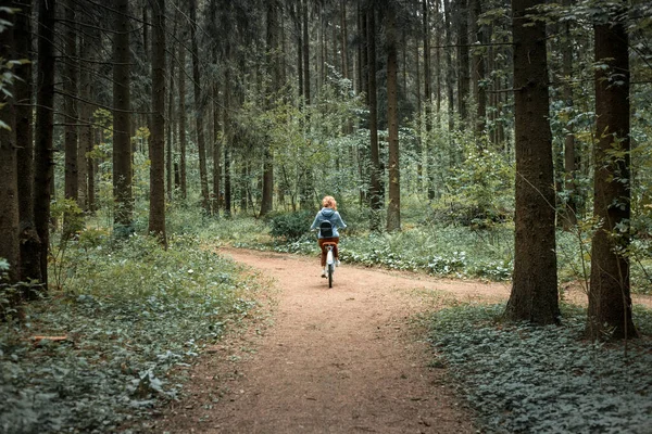 Une femme roule au loin le long d'une route forestière sur un vélo — Photo