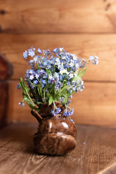 Ramo de flores no me olvides flores en un jarrón de cerámica sobre un fondo de madera. — Foto de Stock
