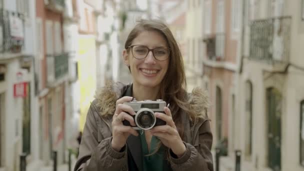 笑みを浮かべて女性観光客が通りに立っている間カメラ目線します ビンテージ カメラを保持している眼鏡の魅力的な若い女性 旅行の概念 — ストック動画