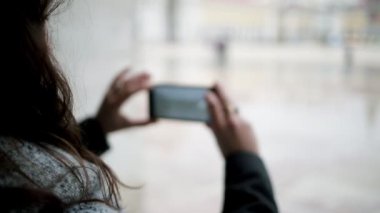 Akıllı telefonlu genç bir kadın ıslak Avrupa şehrinin fotoğraflarını çekiyor.