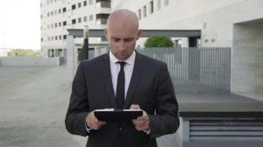 Tatminsiz kel iş adamı tablet üzerinde yazıyor ve yürüyor.