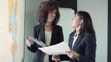 Genç ve güzel iş kadınları raporları tartışıyor ve gülümsüyor.