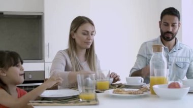 Genç ebeveynler ve küçük kız birlikte kahvaltı ediyorlar.