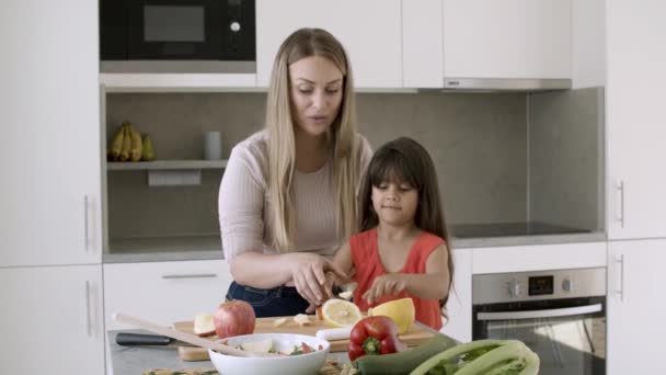 Mamá ayudando a su hijita a cortar verduras para ensalada — Vídeos de Stock