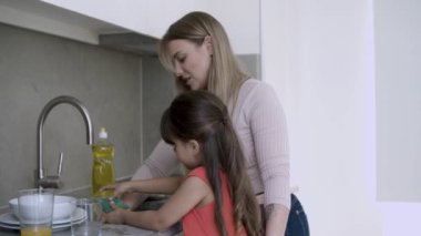 Neşeli anne, kızlara bulaşık yıkamayı öğretiyor.