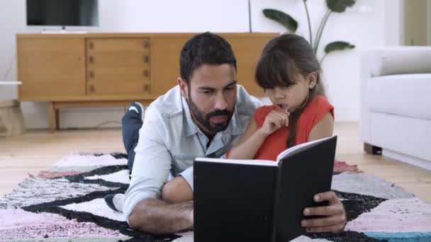 Niña y su padre relajándose en el suelo y leyendo el libro — Vídeos de Stock