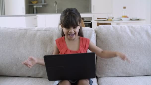 Opgewonden vrolijk klein meisje met behulp van laptop door haarzelf — Stockvideo