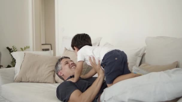 Fröhlicher Papa liegt auf Couch, hält und hebt Sohn — Stockvideo