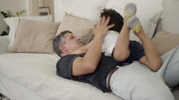 Szczęśliwy tata grać i kołysać się z małym synem na kanapie — Wideo stockowe