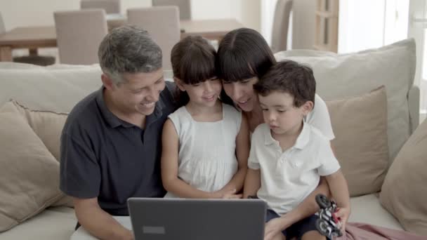 Boldog szülők és két gyerek ül a laptopnál a nappaliban — Stock videók