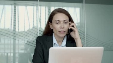 Ciddi kadın proje yöneticisi iş yerinde dizüstü bilgisayarla oturuyor