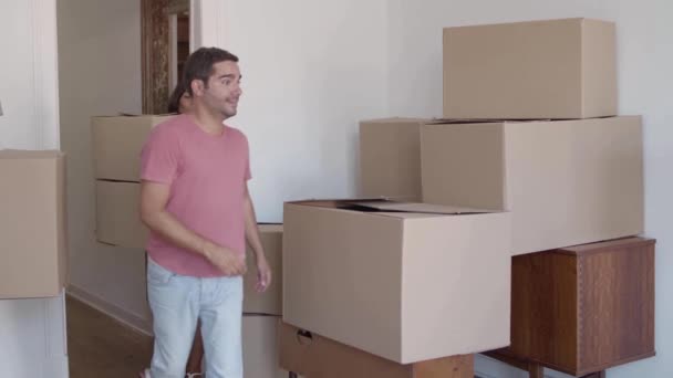 Молодой человек входит в комнату и несет картонную коробку — стоковое видео