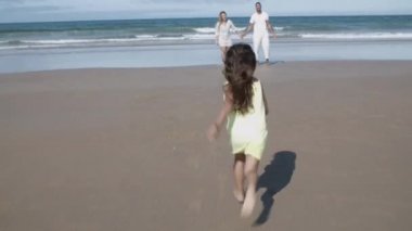 Küçük bir kız sahilde ailesinin kucağına koşuyor.